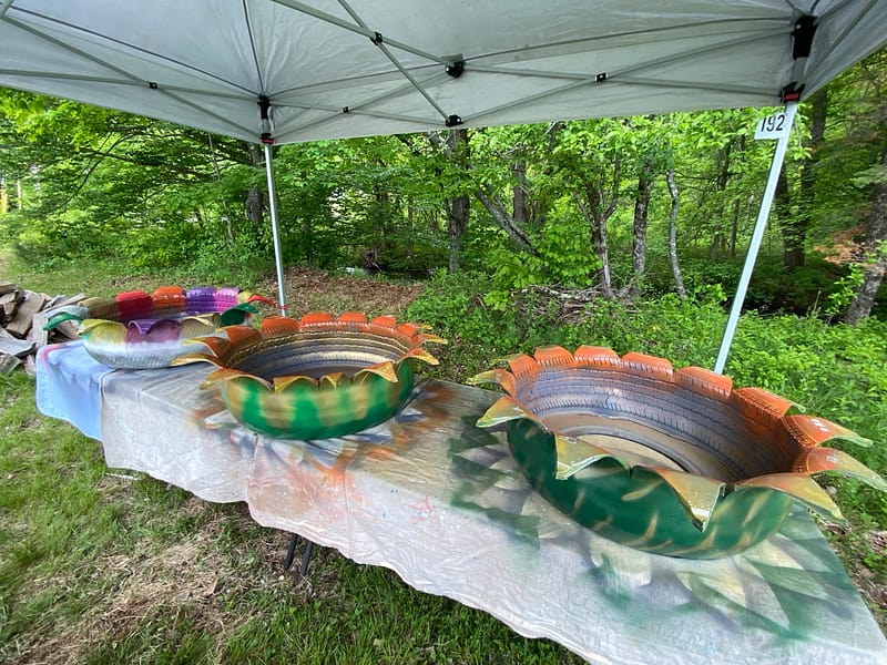 Hand-painted flower-shaped tire planters displayed beside a brook during an outdoor upcycled tire planter workshop in Grafton, New Hampshire.